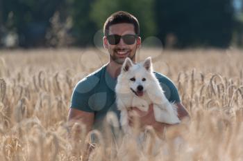 Young Man Sitting With Dog German Spitz In Harvested Field