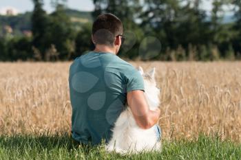 Young Man Sitting With Dog German Spitz In Harvested Field