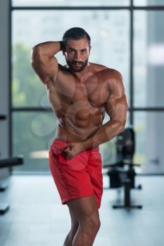 Young Italian Man Standing Strong In The Gym And Flexing Muscles - Muscular Athletic Bodybuilder Fitness Model Posing After Exercises