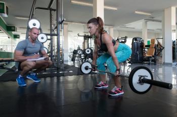 Personal Trainer Showing Young Woman How To Train Back With Barbell In The Gym