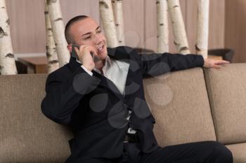 Young Happy Man Sitting Relaxed on Sofa and Talking on the Phone