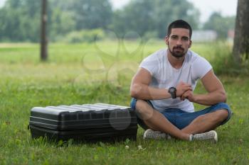 Portrait of Confident Young Engineer Sitting On Grass With Case from Drone