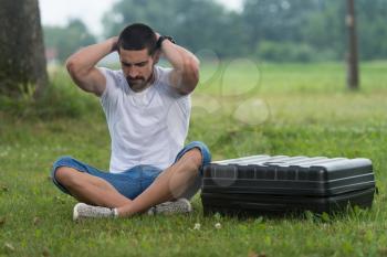 Portrait of Frustrated Young Engineer Sitting On Grass With Case from Drone