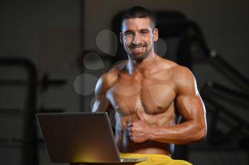 Resting Time - Confident Muscled Young Man Resting In Healthy Club Gym And Using Laptop