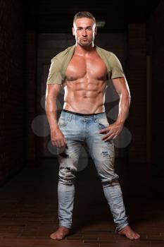Handsome Young Man In Jeans & T-shirt Standing Strong In The Gym And Flexing Muscles - Muscular Athletic Bodybuilder Fitness Model Posing After Exercises