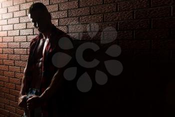 Portrait Of A Young Physically Fit Man Showing His Well Trained Body While Wearing Plaid Shirt - Muscular Athletic Bodybuilder Fitness Model Posing After Exercises On Wall of Bricks