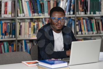 Portrait Of African Clever Student With Open Book Reading It In College Library - Shallow Depth Of Field