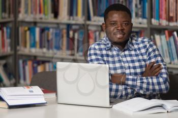 In The Library - Handsome African Male Student With Laptop And Books Working In A High School - University Library - Shallow Depth Of Field
