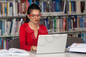 In The Library - Pretty Female Student With Laptop And Books Working In A High School Or University Library - Shallow Depth Of Field