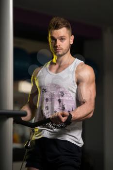 Handsome Muscular Fitness Bodybuilder In Undershirt Doing Heavy Weight Exercise For Biceps On Machine With Cable In The Gym