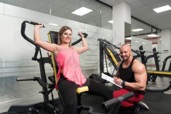 Personal Trainer Showing Young Woman How To Train Shoulders With Dumbbels In The Gym