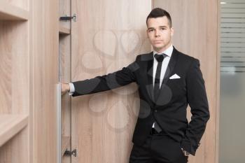 Portrait Of Handsome Confident Young Businessman Standing And Opens Cabinet