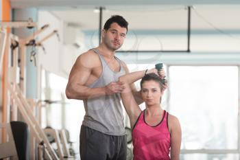 Personal Trainer Showing Young Woman How To Train Triceps Exercise With Dumbbell In A Health And Fitness Concept