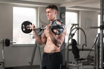 Young Athlete In The Gym Performing Biceps Curls With A Barbell