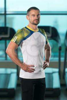 Personal Trainer Standing Strong In Fitness Centar - Gym Background With Copyspace And Flexing Muscles - Muscular Athletic Man Posing