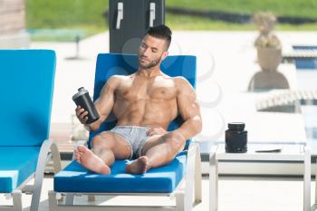 Young Man Resting On Sun Loungers By Swimming Pool With Supplements Pills And Dope or Shaker for Copy Space - a Place for Your Text