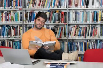 In the Library - Handsome Male Student With Laptop and Books Working in a High School - University Library - Shallow Depth of Field