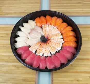 Assortment of fresh sushi placed neatly in a large plastic plate with bamboo place mats underneath on glass table