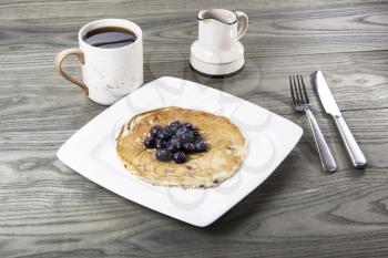 Pancakes with Blueberries on top, cup of coffee, utensils, on aging wood background