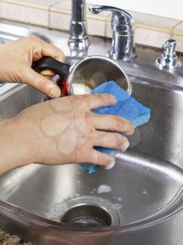 Vertical photo of female hands cleaning a coffee mug with soapy water and a sponge with kitchen sink in background