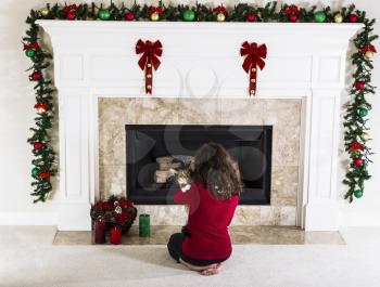 Young girl holding family cat in front of holiday decorated natural gas fire place in living room of home