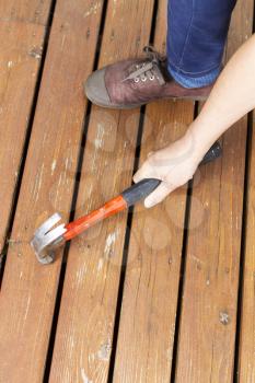 Vertical photo of female hand, work shoes, and hammer adjusting boards, on a natural faded cedar wood deck