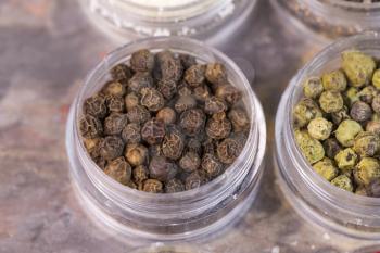 Horizontal top focus shot of dark brown peppercorns in small containers on stone surface