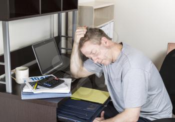 Mature man holding head in hand with computer, tax income booklet and coffee cup on desk
