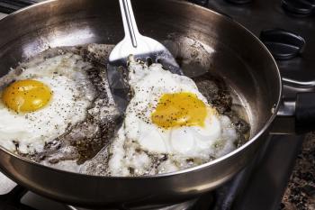 Eggs in frying pan being cooked by bacon grease with spatula