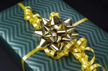 Gift box with yellow ribbons and golden bow on black background
