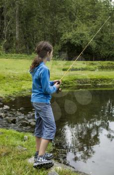 Young girl fishing in small lake with woods in background