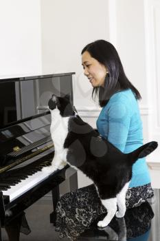 Vertical photo of mature woman playing piano with family cat at her side