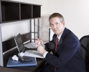 Mature Man crushing paper in hands with calculator, computer and papers on desk