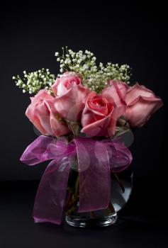 Pink roses with small white flowers in glass vase on dark background