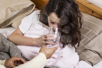 Young sick girl in bed getting glass of water from mom
