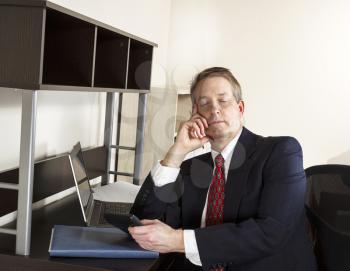Mature man sleeping at office with calculator in hand and computer and papers on desk