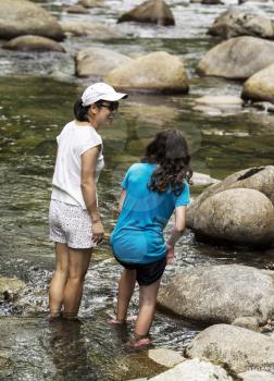 Mother and daughter wading in stream with large rocks and water in background