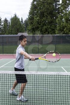 Young Asian Man using backhand volley on outdoor tennis court