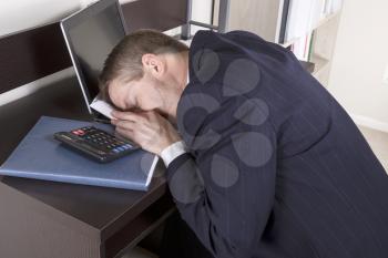 Mature Man resting his head on tax booklet with calculator, papers and computer on desk