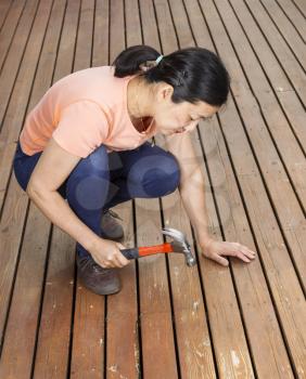 Vertical photo of mature woman adjusting boards, with hammer in raised position, on a natural faded cedar wood deck