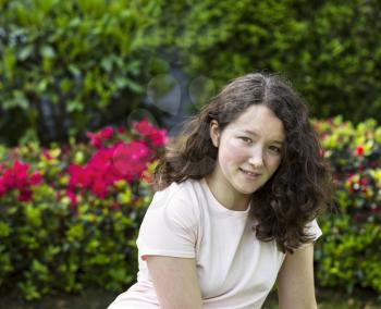 Photo of young girl sitting in front of flowering bushes with a smile on a nice day outdoors