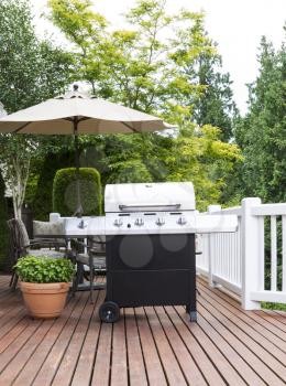 Vertical photo of large barbecue cooker on cedar deck with patio furniture and trees in background  