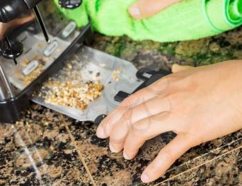 Photo of female hand cleaning bottom of kitchen toaster tray with green microfiber rag with stone counter top in background  