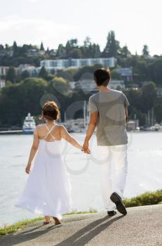 Vertical photo of young adult couple walking on path with harbor in Background