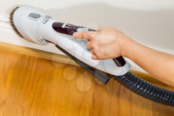 Horizontal photo of female hand with vacuum cleaner brush extension cleaning trim work near wooden floors