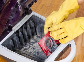 Photo of gloved hands completing cleanup of inside of vacuum cleaner with hardwood floors in background 