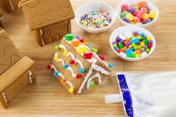 Horizontal photo of parts of Gingerbread houses being assembled with ingredients on top of natural bamboo cutting board 