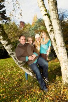 Vertical photo of family resting on trees, with man in forefront, during a lovely day in autumn