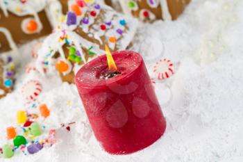 Closeup angled horizontal photo of red candle with Gingerbread houses, surrounded by powdered snow in background 