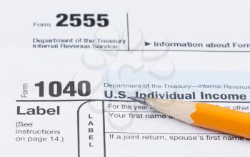 Closeup horizontal photo of pencil resting on IRS Tax Forms 1040 and 2555